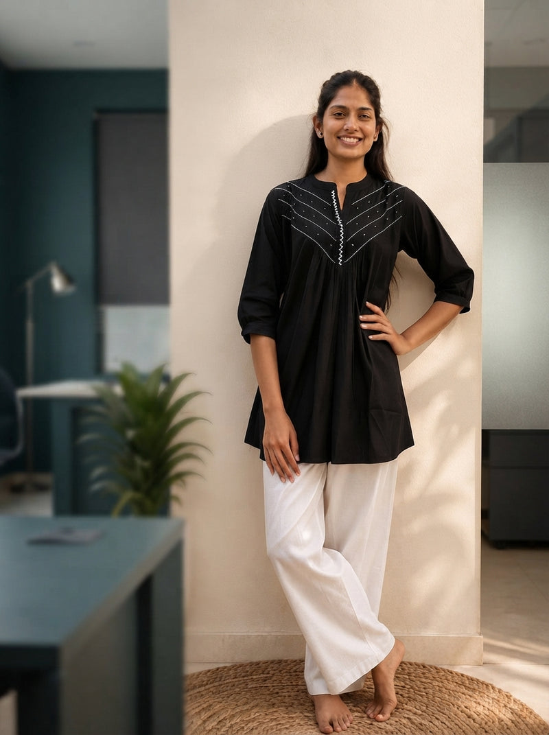 A woman wearing a black kurti in a modern office with a blurred, minimalist background.